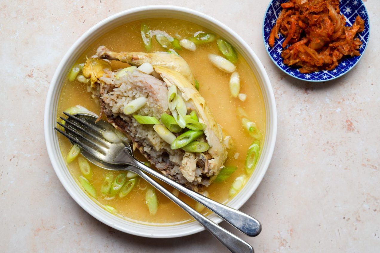 Bowl of Korean Chicken Ginseng Soup with a dish of kimchi on the side.