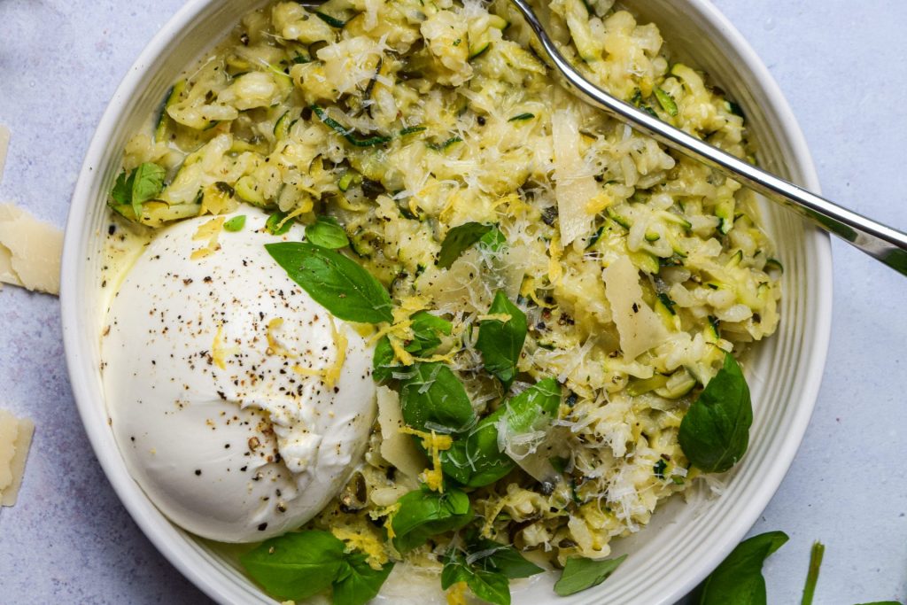 Close up of a bowl of courgette risotto with fresh basil and a ball of burrata.
