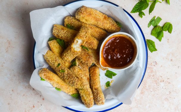 Blue and white bowl of air fryer halloumi fries with a bowl of chilli ketchup for dipping.