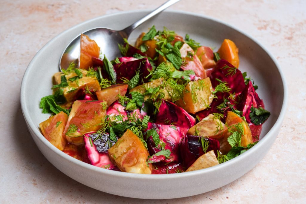 Grey bowl of Greek beetroot and yogurt salad with fresh herbs scattered on top.