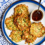 Plate of courgette halloumi fritters on a blue and white tile background.