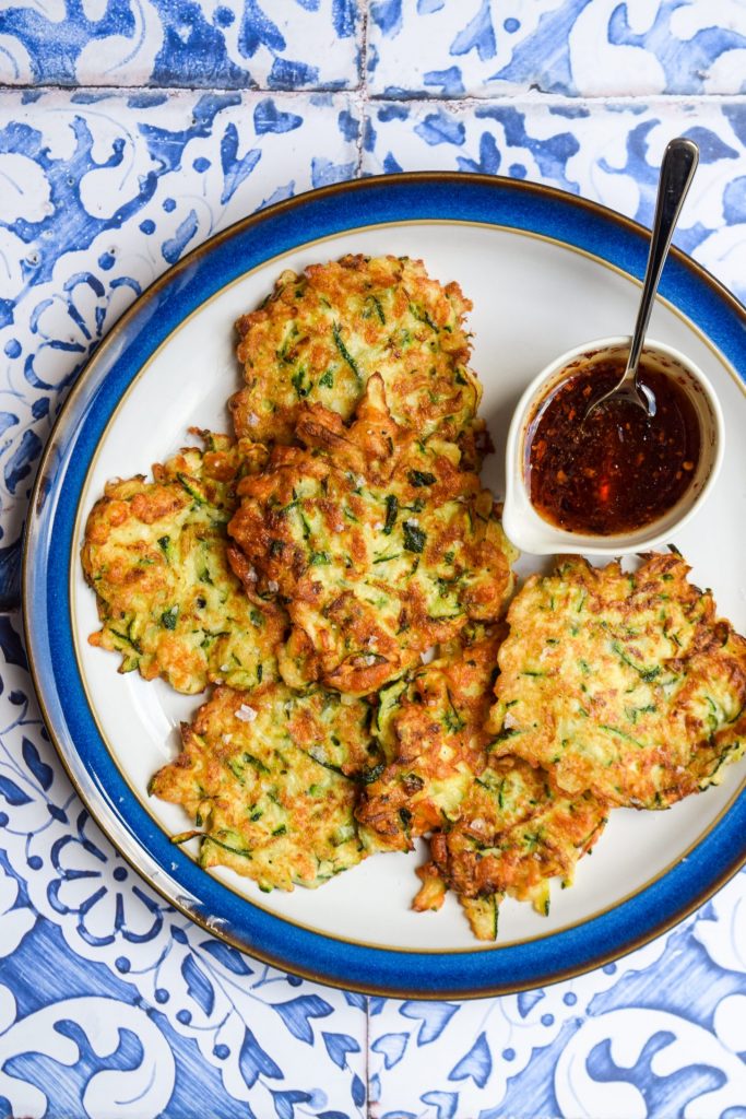 Plate of courgette halloumi fritters on a blue and white tile background.