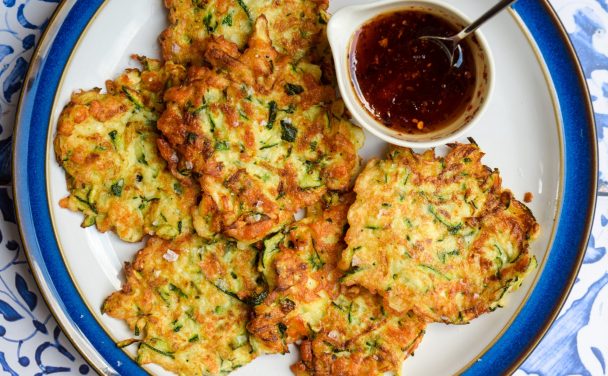 Courgette halloumi fritters with a bowl of hot honey on a blue and white plate.