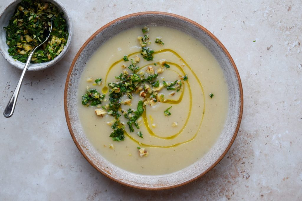 Bowl of celeriac soup topped with walnut gremolata with a small bowl of gremolata to one side.