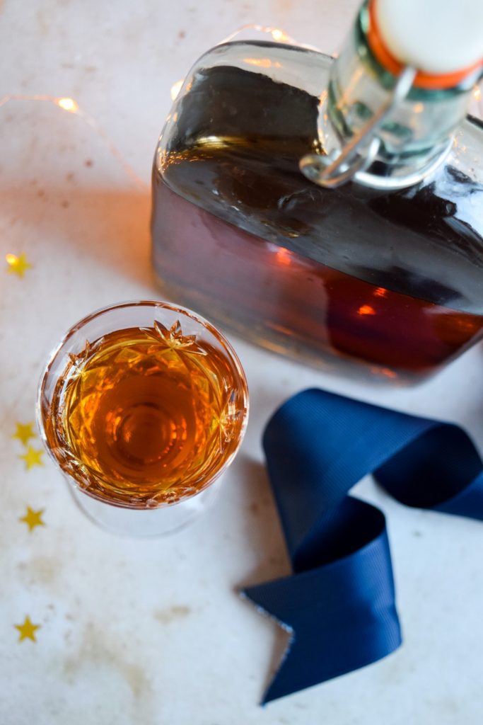 Bottle and glass of homemade amaretto on a gold star strewn background.