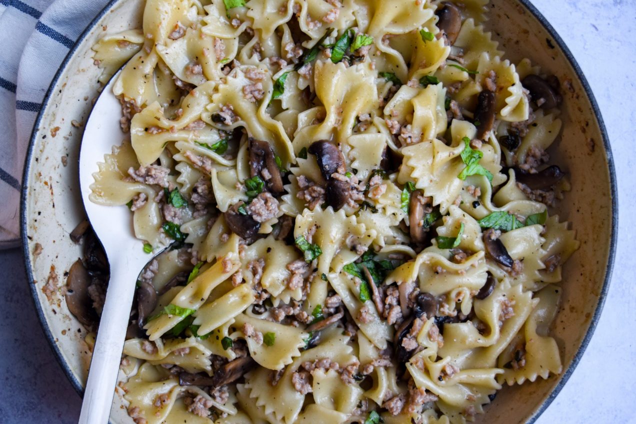 Close up of a pan of pasta bowls with mushrooms, pork and basil.