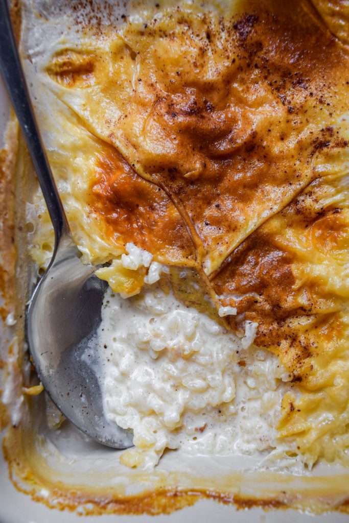 Close up of a dish of baked rice pudding with a golden skin and a silver spoon taking out a spoonful.
