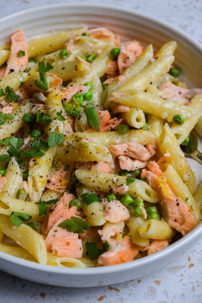 Salmon and pea pasta in a white bowl.