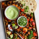 Roasted veggies on a sheet pan with a bowl of avocado crema.