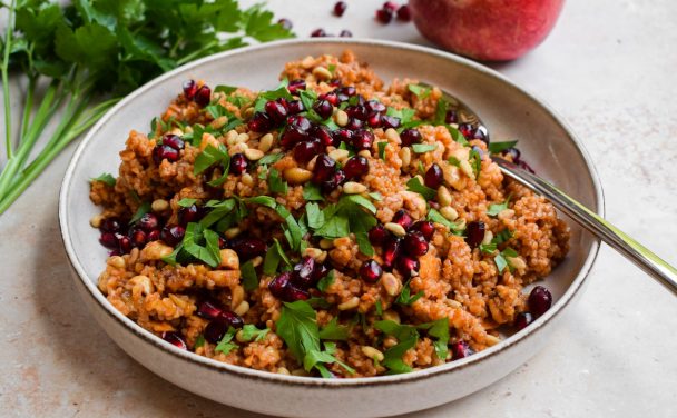 Stone coloured bowl of bulgar wheat salad scattered with pomegranates.