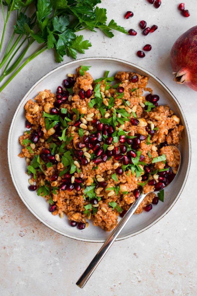 Close up of a tomato dressed bulgur wheat salad with parsley and pomegranate.