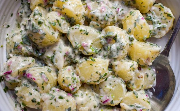 Close up of a bowl of creamy potato salad with red onions and herbs.