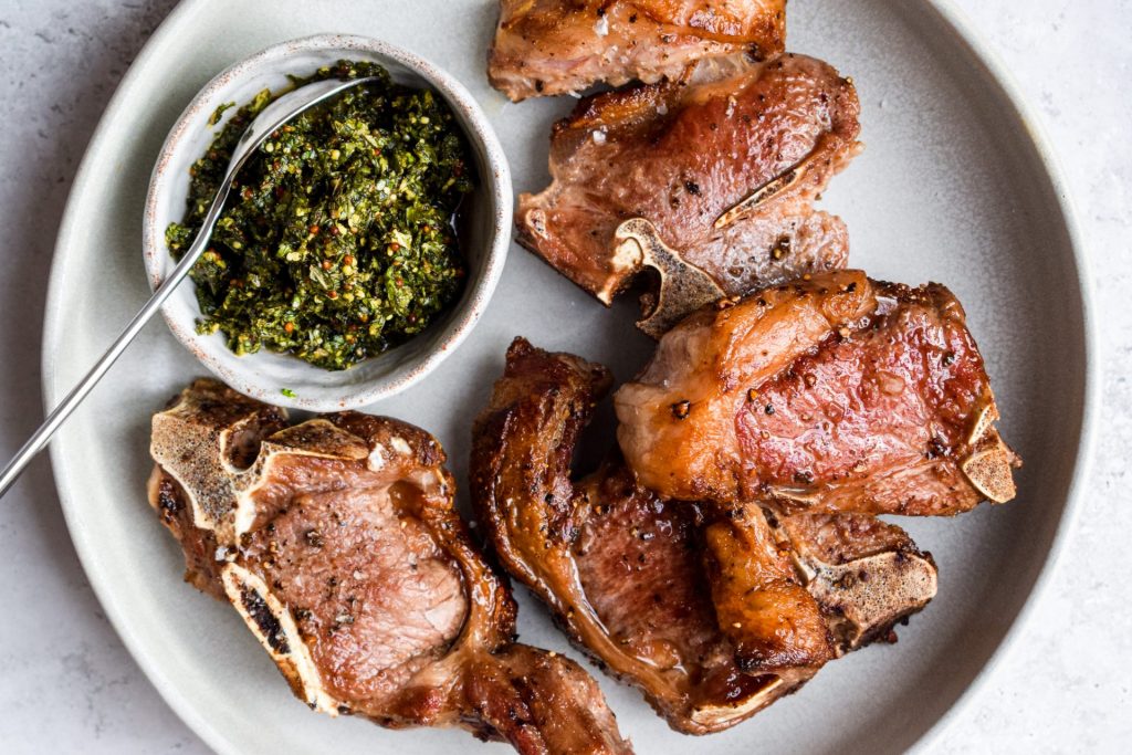 Grey plate with pan fried chops and a grey bowl of fresh mint sauce.
