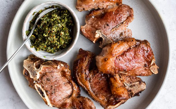 Grey plate with pan fried chops and a grey bowl of fresh mint sauce.