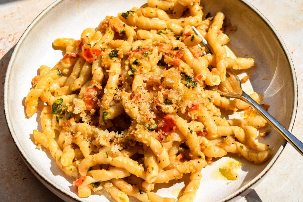 Close up of a bowl of tomato and almond pesto pasta topped with toasted breadcrumbs.