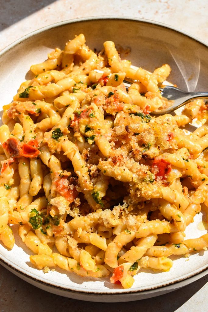Plate of pasta with Sicilian tomato and almond pesto with toasted breadcrumbs pictured in direct sunlight.