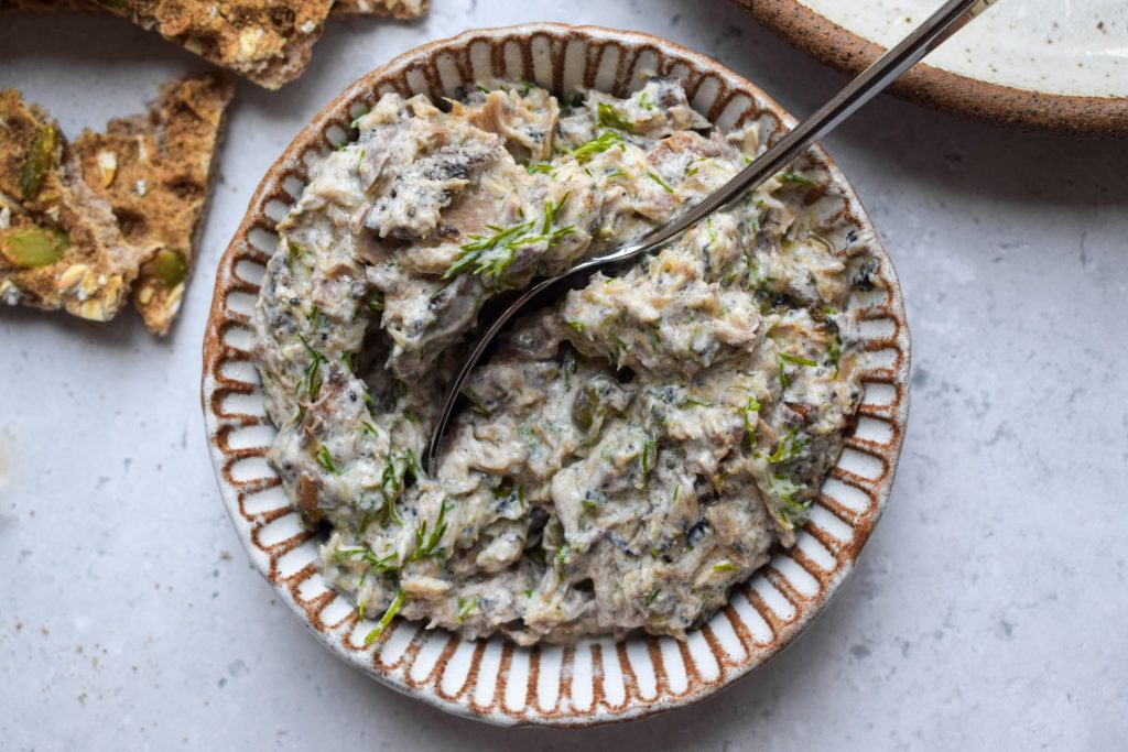 White bowl of mackerel pate topped with fresh dill on a grey background.
