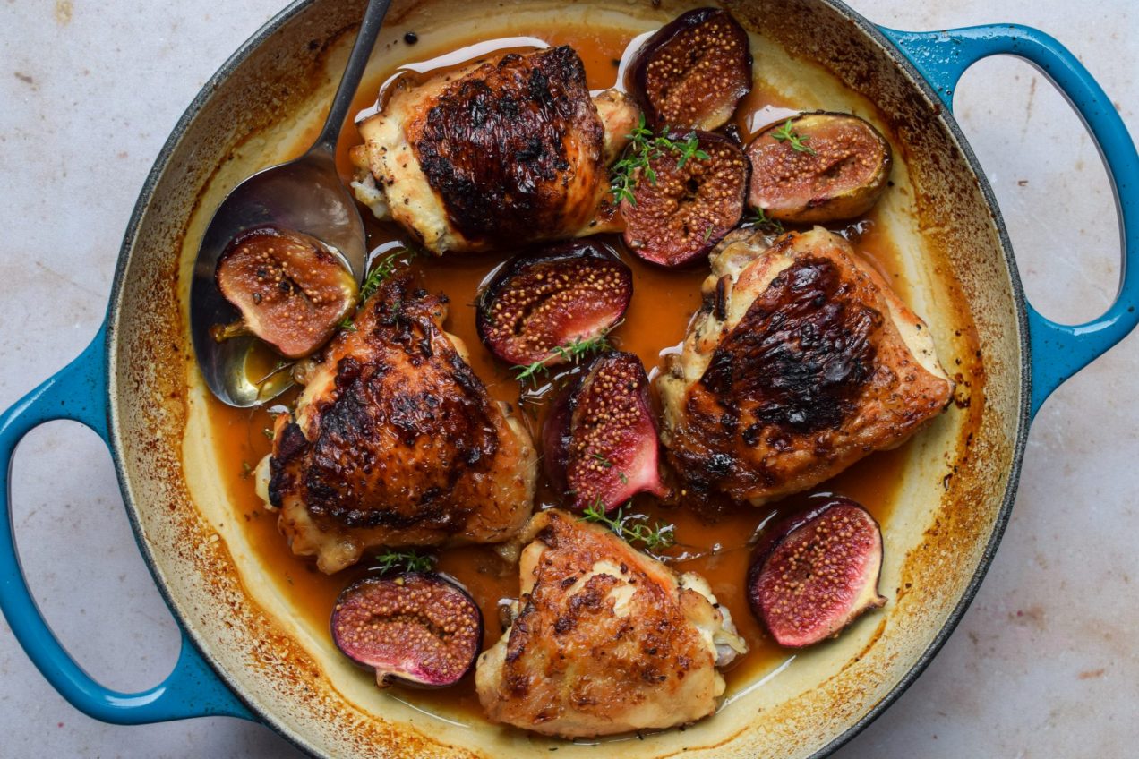 Close up of a blue casserole dish of roasted chicken thighs with figs,.
