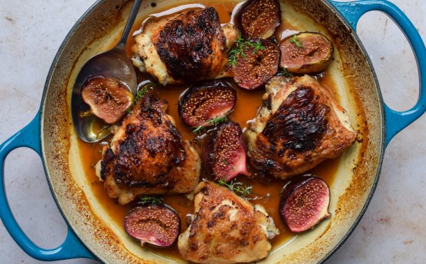 Close up of a blue casserole dish of roasted chicken thighs with figs,.