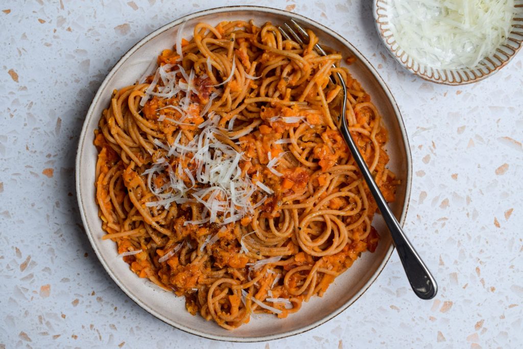 Bowl of orange spaghetti with a dish of grated cheese on the side.