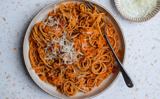 Bowl of orange spaghetti with a dish of grated cheese on the side.