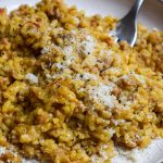 Plate of sausage and saffron risotto sprinkled with grated parmesan.