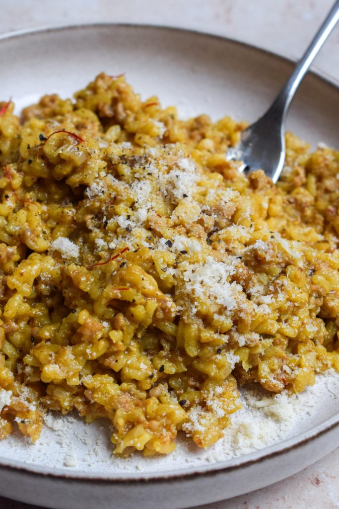 Plate of sausage and saffron risotto sprinkled with grated parmesan.