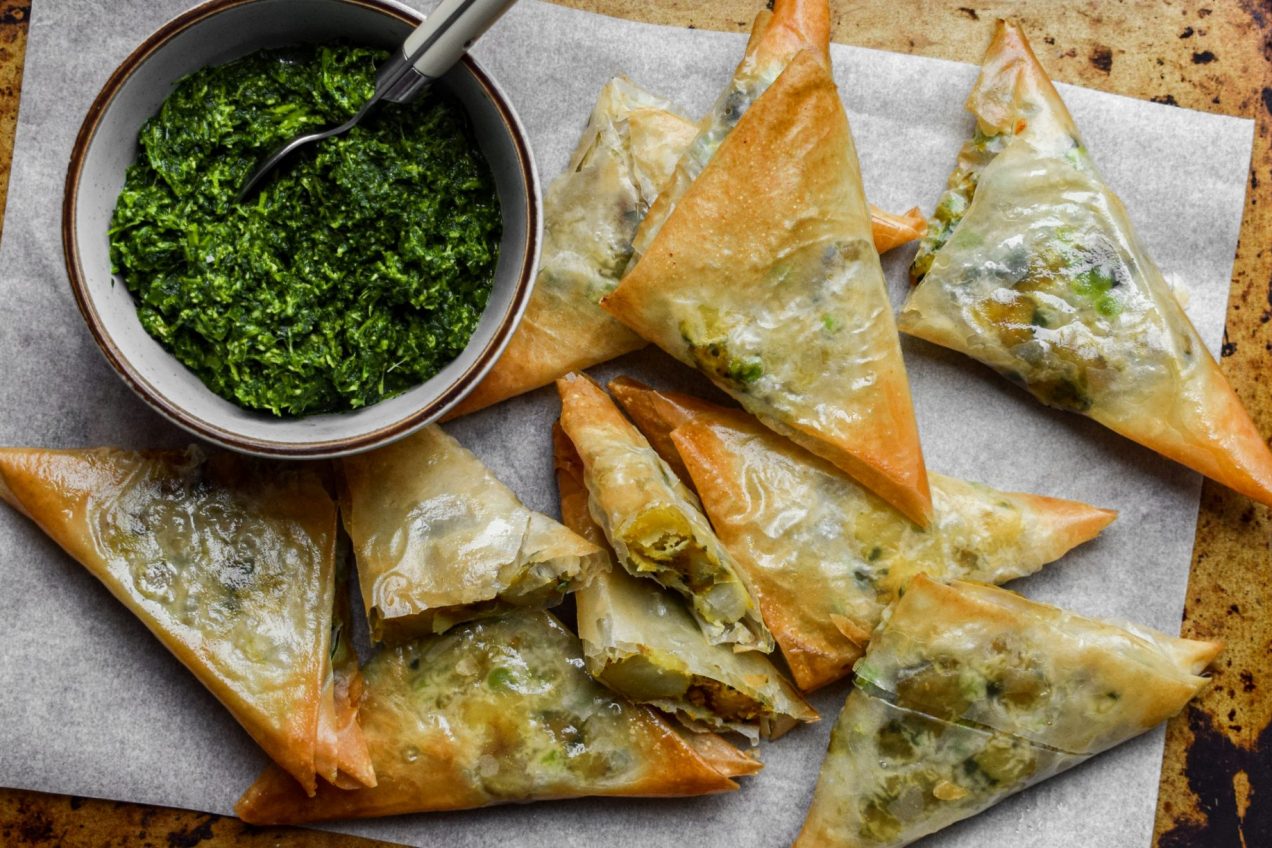 Filo samosas on a piece of baking parchment next to a bowl of chutney.