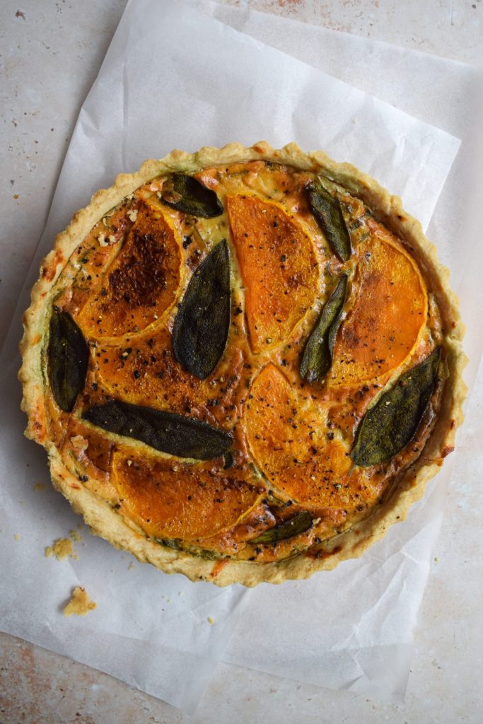 Sage and squash tart on a neutral stone background.