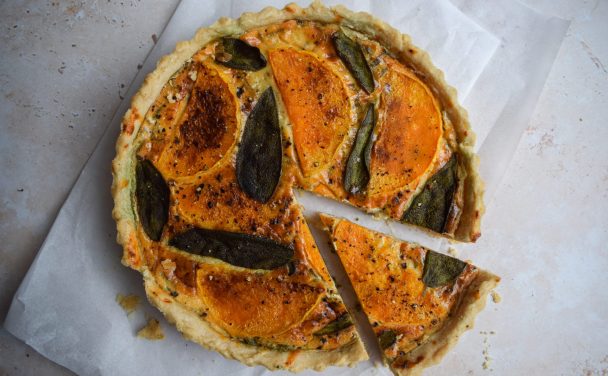 Squash tart topped with sage leaves on a piece of baking parchment.