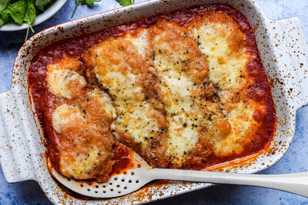 Close up of a baking dish of chicken parm with a green salad on the side.