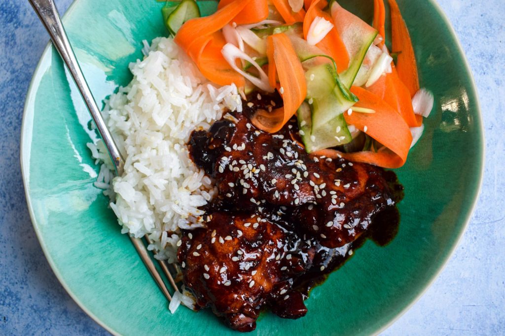 Blue bowl of Korean chicken, rice and pickled vegetables.