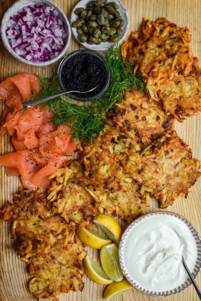 Close up of latkes with soured cream, smoked salmon, chopped onion, capers, dill, lemon wedges and lumpfish caviar.