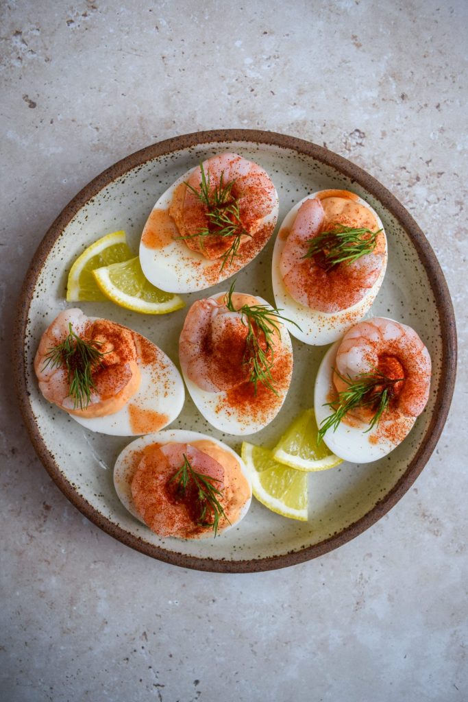 Plate of devilled eggs topped with prawns and paprika.