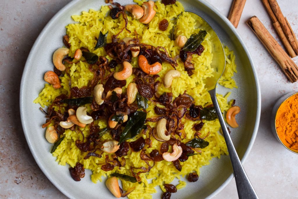 Plate of yellow rice topped with cashews and onions.