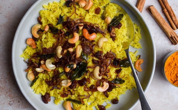 Plate of yellow rice topped with cashews and onions.