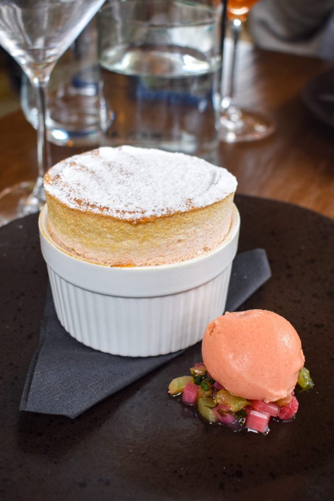 Rhubarb soufflé on a black plate with a scoop of blood orange sorbet. 