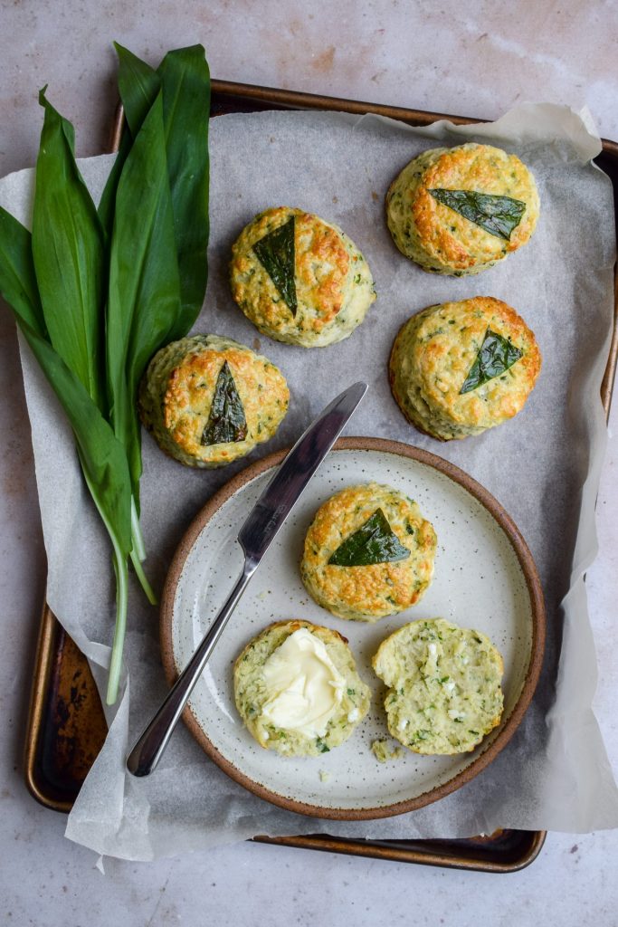 Tray of wild garlic scones with one split open on a plate and spread with butter.
