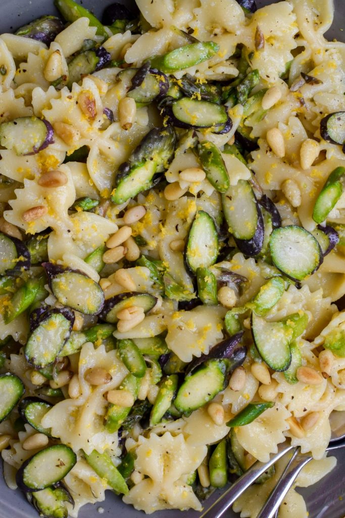 Close up of a pasta salad with asparagus, lemon and pine nuts.