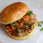 A pork burger with a carrot and daikon slaw on a folded piece of baking parchment.