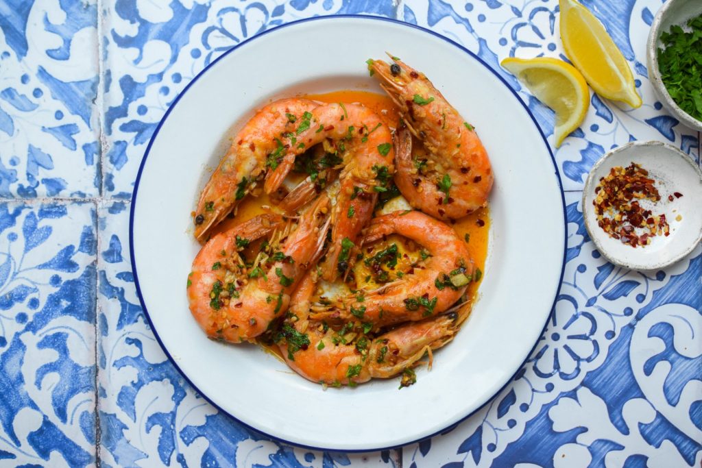 Pil Pil Prawns on a blue and white plate with lemon wedges on the side for serving.