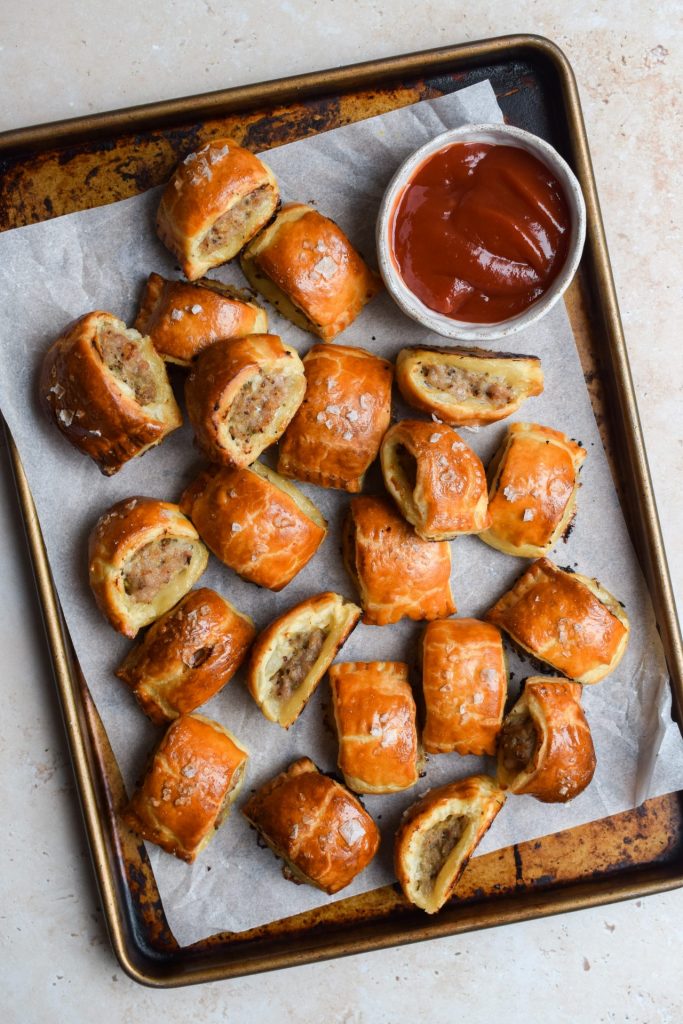 A tray of honey mustard sausage rolls with a bowl of tomato sauce for dipping.