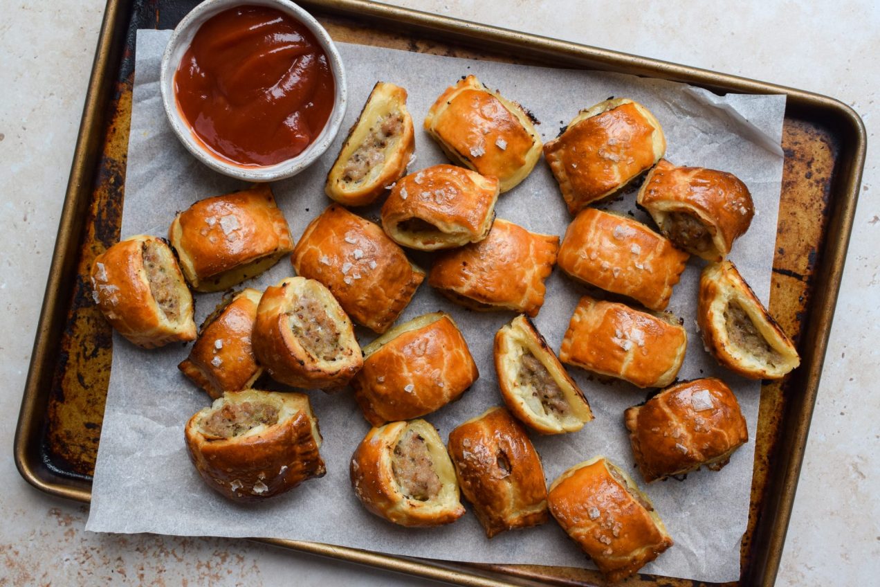 A tray of sausage rolls with a bowl of ketchup for dipping.