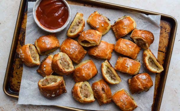 A tray of sausage rolls with a bowl of ketchup for dipping.
