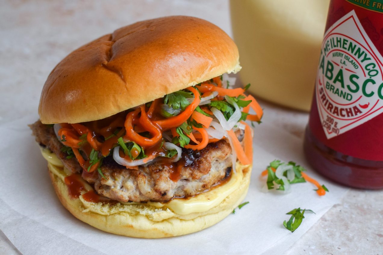 A Pork Banh Mi Smash Burgers next to a bottle of Tabasco sriracha.