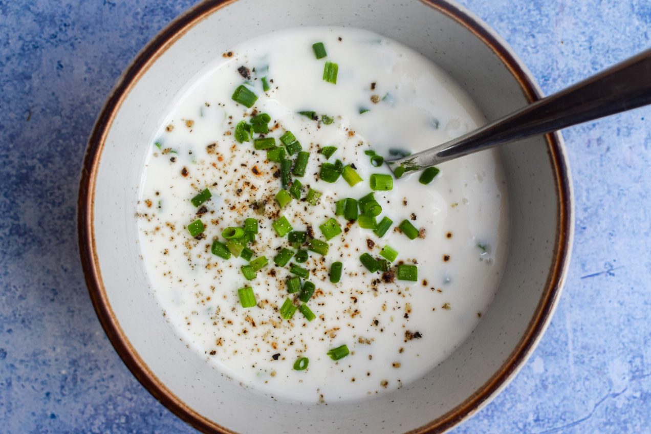 Close up of a bowl of ranch dressing garnished with chopped chives with a spoon sticking out of it.