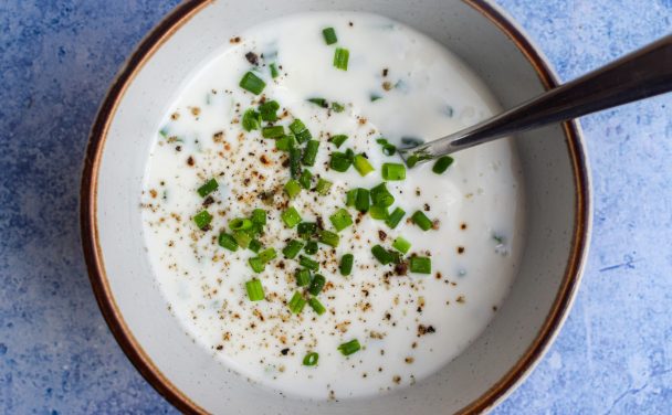 Close up of a bowl of ranch dressing garnished with chopped chives with a spoon sticking out of it.