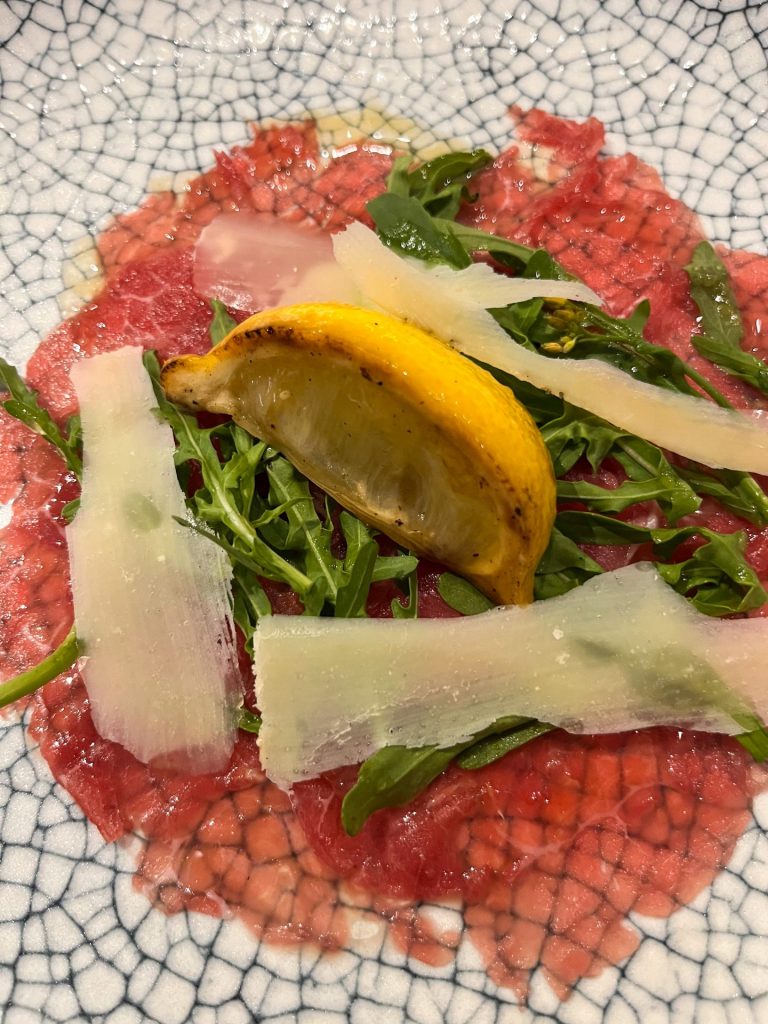 Close up of beef carpaccio with shaved parmesan, rocket and a lemon wedge,