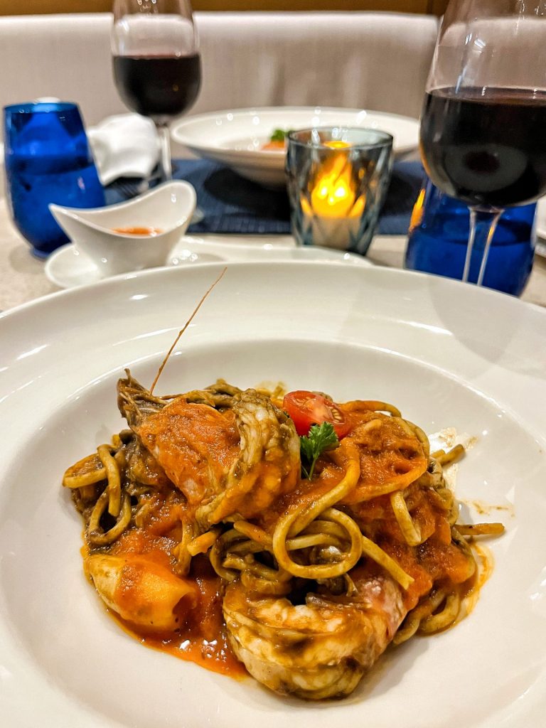 White plate of seafood spaghetti with glasses of red wine in the background.