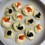 A grey plate of crisps topped with sour cream and black and orange caviar.